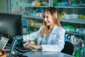 Attractive female pharmacist in uniform working on pc computer using keyboard in pharmacy