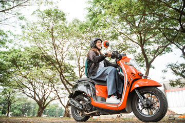 High school girl wearing helmet and jacket riding motorbike to school