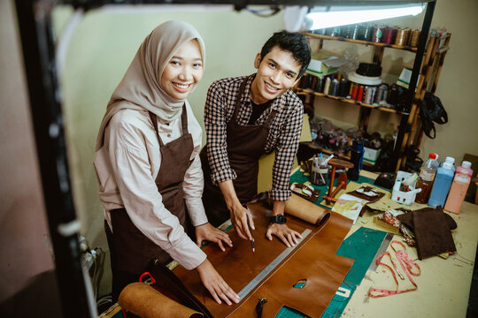 craftsman and craftswoman in hijab smiling at the camera in a leather workspace