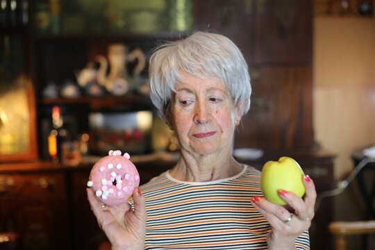Senior woman deciding between apple or doughnut 