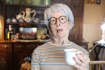 Grumpy looking senior woman holding coffee cup 