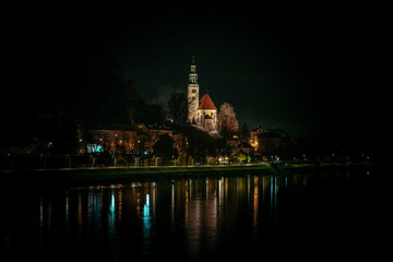 Fototapeta na wymiar Müllner Church in Salzburg, Austria, at night with lights from the banks of the Salzach river