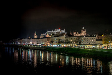 Salzburg old town with Fortress Hohensalzburg in the background at night with lights from the banks of the Salzach river in Austria 