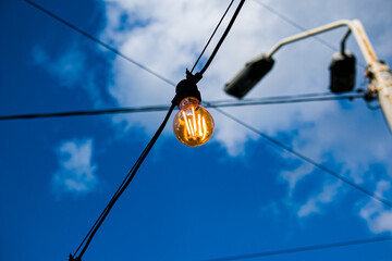 Close up of an Edison-style filament on a light bulb against a cloudy sky. Energy crisis.