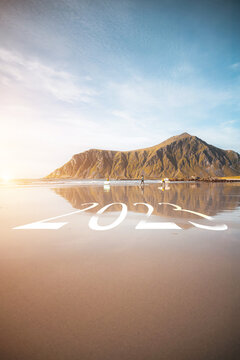 Happy New Year 2023 text on island beach sand and water reflections. Sea sunset in Lofoten Islands, Norway.