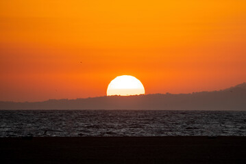 Scenic and tranquil view of seascape and beautiful bright sun setting down behind silhouette...