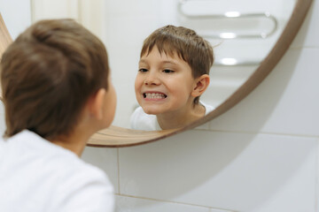 cute 8 years old boy washing face in bathroom looking in mirror and smiling. 