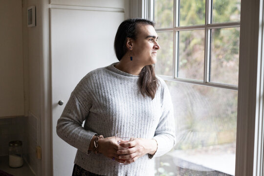 Non-binary person smiling and looking out of the window.