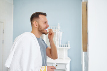 Man brushing teeth in bathroom looking at mirror side view shot