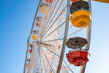 Low angle view of of colorful ferris wheel with clear blue sky in background during summer season at Pacific Park on Santa Monica Pier at Los Angeles - Powered by Adobe