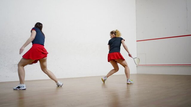 Sportive female opponents compete playing squash on court