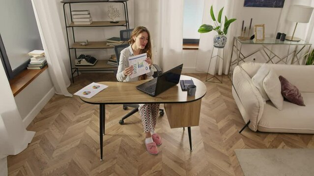 Home office, woman works with computer and documents. A girl in pajamas and slippers sits at the table and does business. Remote work, quarantine. High quality 4k footage