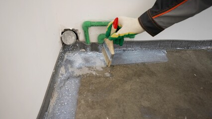 Floor waterproofing membrane on concrete floor. On the floor, the master applies white waterproofing. Floor waterproofing, hands close-up.