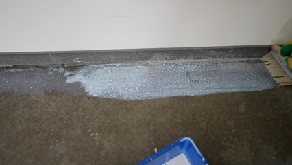 Naklejka premium Grounding the floor, preparing the floor for laying mortar. A worker applies a primer to the floor with a brush.