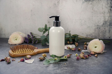   Natural homemade shampoo or wash gel in white pump bottle on grey background with hairbrush, flowers and eucalyptus. Natural skin care. 