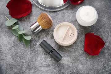 Obraz na płótnie Canvas Natural homemade lipstick and face loose powder with blush (powder brush) on grey marble background with eucalyptus leaves and red rose petals. 