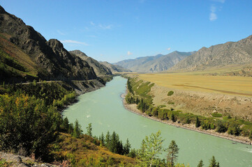 A bend of a turquoise river flowing at the foot of high mountains through a picturesque valley.