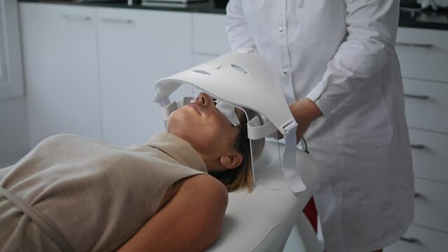 Cosmetologist doing skin treatment turning on led mask in beauty clinic close up