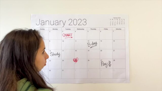 Woman planning a new month by writing on a 2023 wall calendar with a black marker