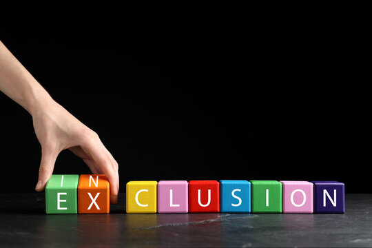 Woman making word Inclusion with colorful cubes on marble table against black background, closeup. Space for text