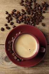 Cup of hot aromatic coffee and roasted beans on wooden table, flat lay
