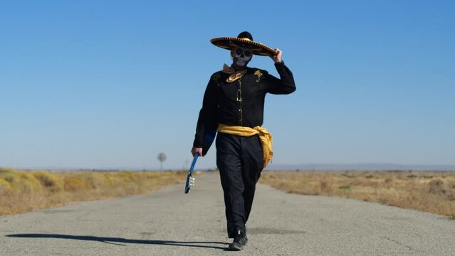 Man in Day of the Dead Costume Walking Down Road in Desert carrying Guitar
