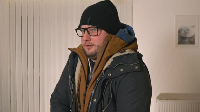 Cold male fastening multiple warm jackets during cost of living crisis in freezing home