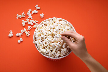 Woman taking fresh popcorn from bucket on orange background, above view