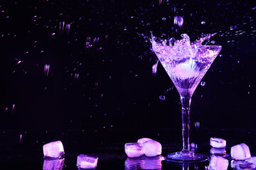 Glass of martini with ice and splashes in neon lights on dark background. Space for text