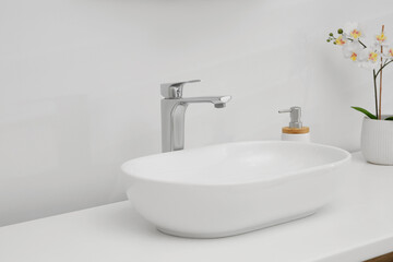 Naklejka na ściany i meble White washbasin, orchid flowers and soap dispenser in bathroom. Interior design
