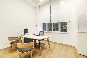 White office table with swivel chair, pc with screen on mast and wooden chairs for visitors