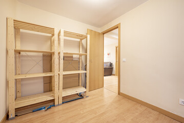 An empty room with empty cargo shelves made of unvarnished wood and a laminate floor with a door of the same material