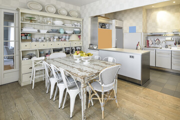 Open kitchen with office with large stripped wooden table with wooden cupboard filled with dishes and pots and wooden flooring