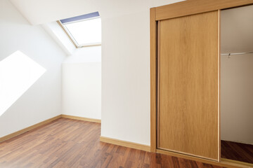 A room on the attic floor with sloping ceilings with skylights with blinds and a built-in wardrobe...