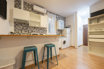 Open kitchen with pine wood top on an island, high blue metal stools, furniture with wooden handles and integrated appliances