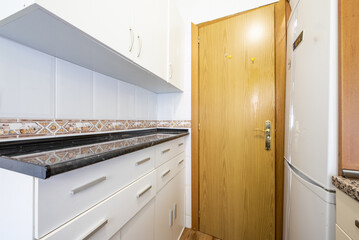 Small narrow kitchen with countertop over lots of white drawers with metal handles and black oak wood door