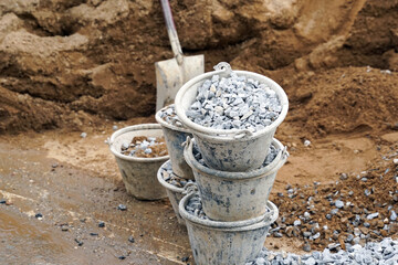 Stone buckets are stacked near the pile of sand to prepare for mixing with cement and other...
