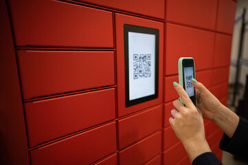 A woman scans a red code to pick up a parcel at a parcel machine. Automated Postal Box.