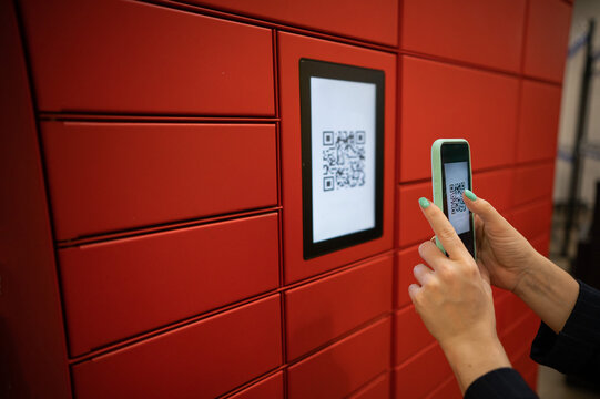 A woman scans a red code to pick up a parcel at a parcel machine. Automated Postal Box.