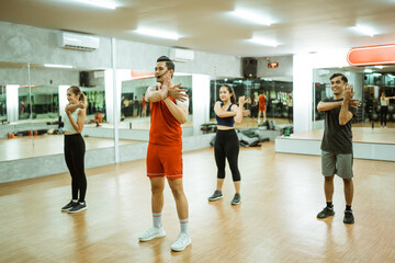 Group of asian men and women in sportswear stretching with instructor in fitness center