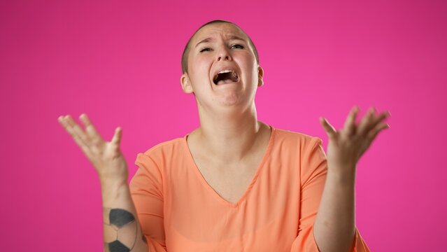 Angry, scared young gender fluid non binary woman 20s put hands on head screaming crying ask why me, isolated on pink background studio.
