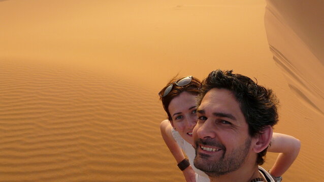 A young couple taking a self picture while climbing to the top of the named "Great Sand Dune" in the red dune sea of Erg Chebbi, Morocco.