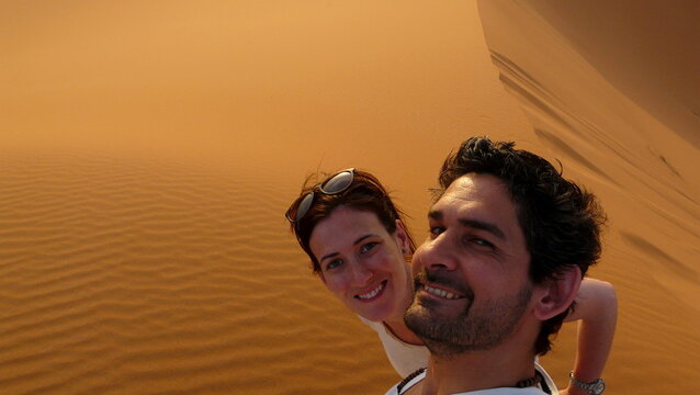 A young couple taking a self picture while climbing to the top of the named "Great Sand Dune" in the red dune sea of Erg Chebbi, Morocco.