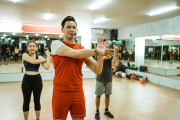 male instructor leading exercise with arm muscle stretching movements in fitness center