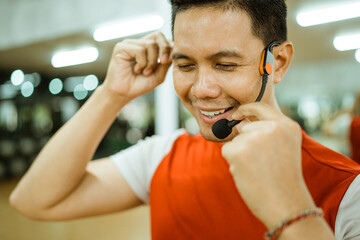 asian male instructor using wireless microphone while preparing before workout in fitness center