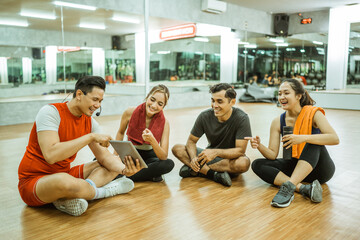 group of young Asian athletes chatting and using a tablet during a break with an instructor