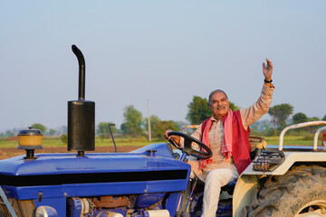 Indian farmer sitting on tractor and giving expression at agriculture field.