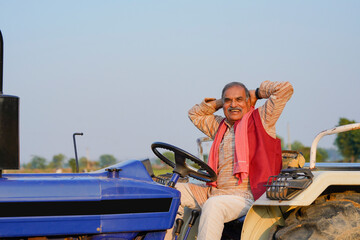 Indian farmer sitting on tractor and giving expression at agriculture field.