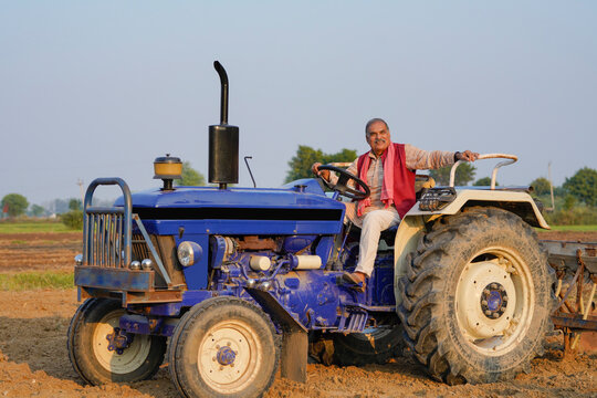 Indian farmer sitting on tractor and giving expression at agriculture field.