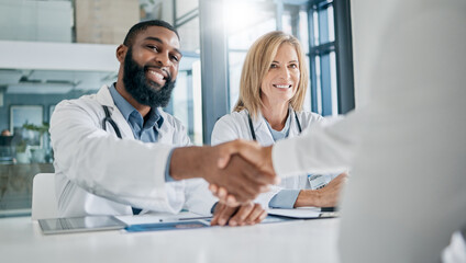 Handshake, partnership or happy doctors in a meeting after successful medical surgery or reaching healthcare goals. Teamwork, woman or black man smiles shaking hands with a worker in hospital office